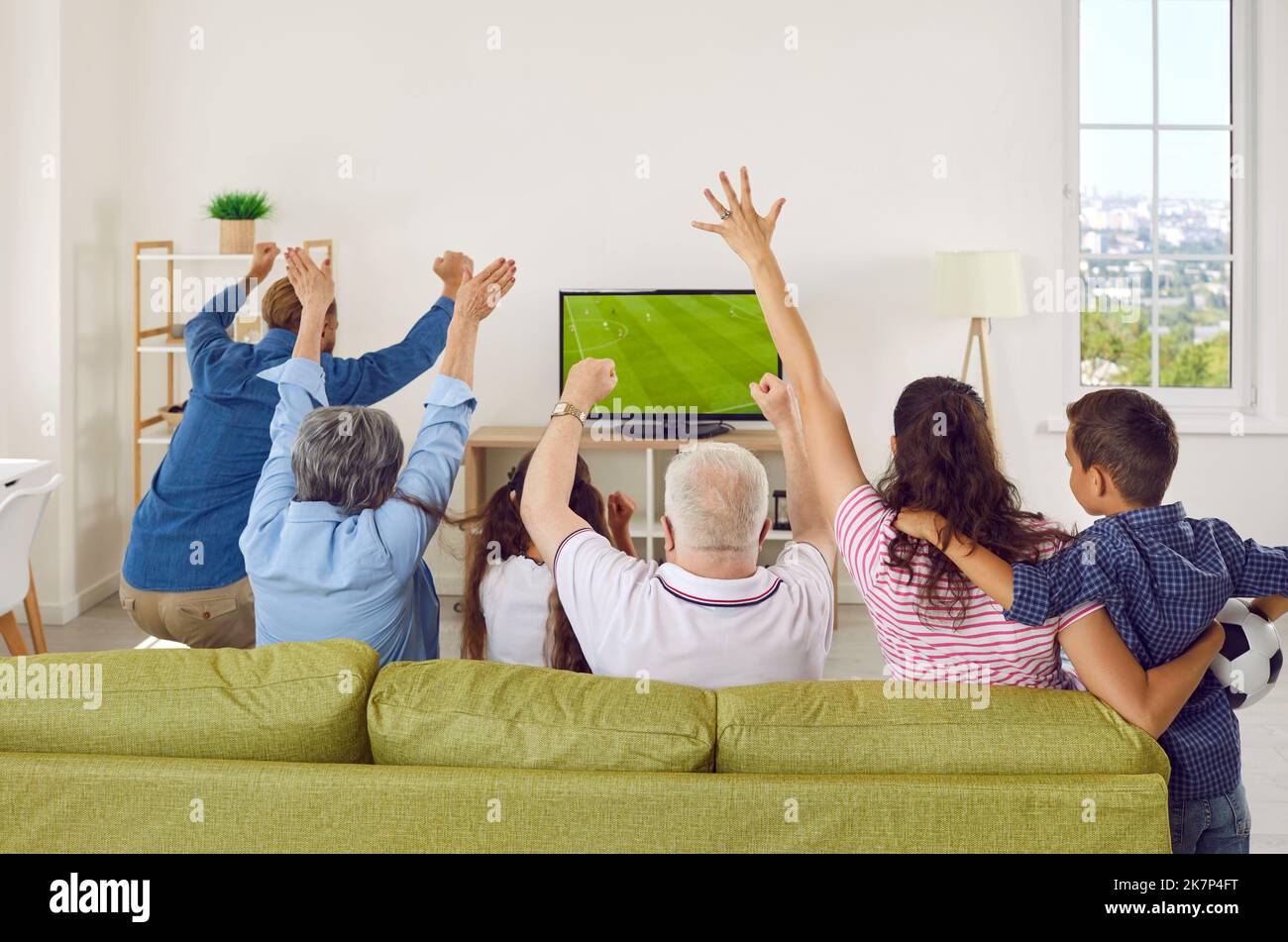 Back view of happy family sitting on sofa at home and watching football match on TV Stock Photo