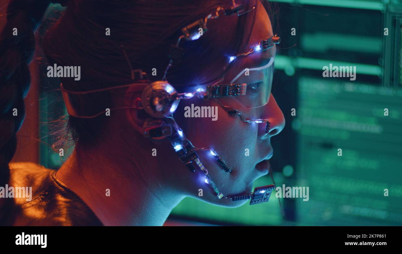 Side view of an Asian girl with futuristic headset and microphone programming using multiple computer screen. Cyperpunk style. Sci-fi background. Stock Photo