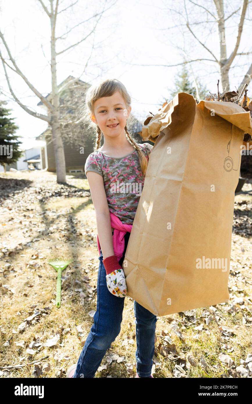 Portrait of cheerful girl carrying full bin liner in backyard Stock