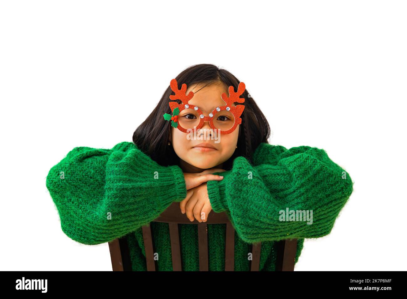 Cute asian child girl in green sweater and masquerade christmas glasses with deer horns. Beautiful Korean girl look at the camera, smiling, the concep Stock Photo