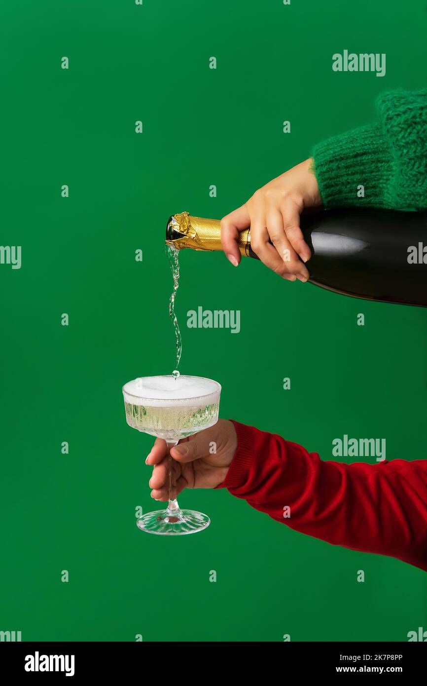 Abstract background of the Christmas party, Champagne is poured from a bottle into a glass in a female hand. Minimalism, green background, Christmas a Stock Photo