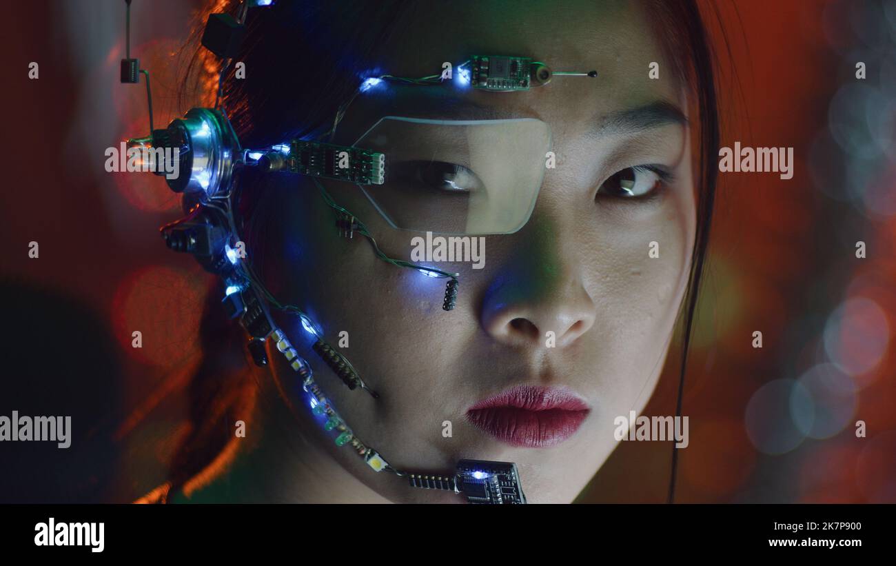 A Cyberpunk girl wearing a headset with microphone, one-eye glasses and white small LED lights. Red neon lights in the background. Asian girl in cyberpunk attire. Cyber and sci-fi backgrounds. Stock Photo