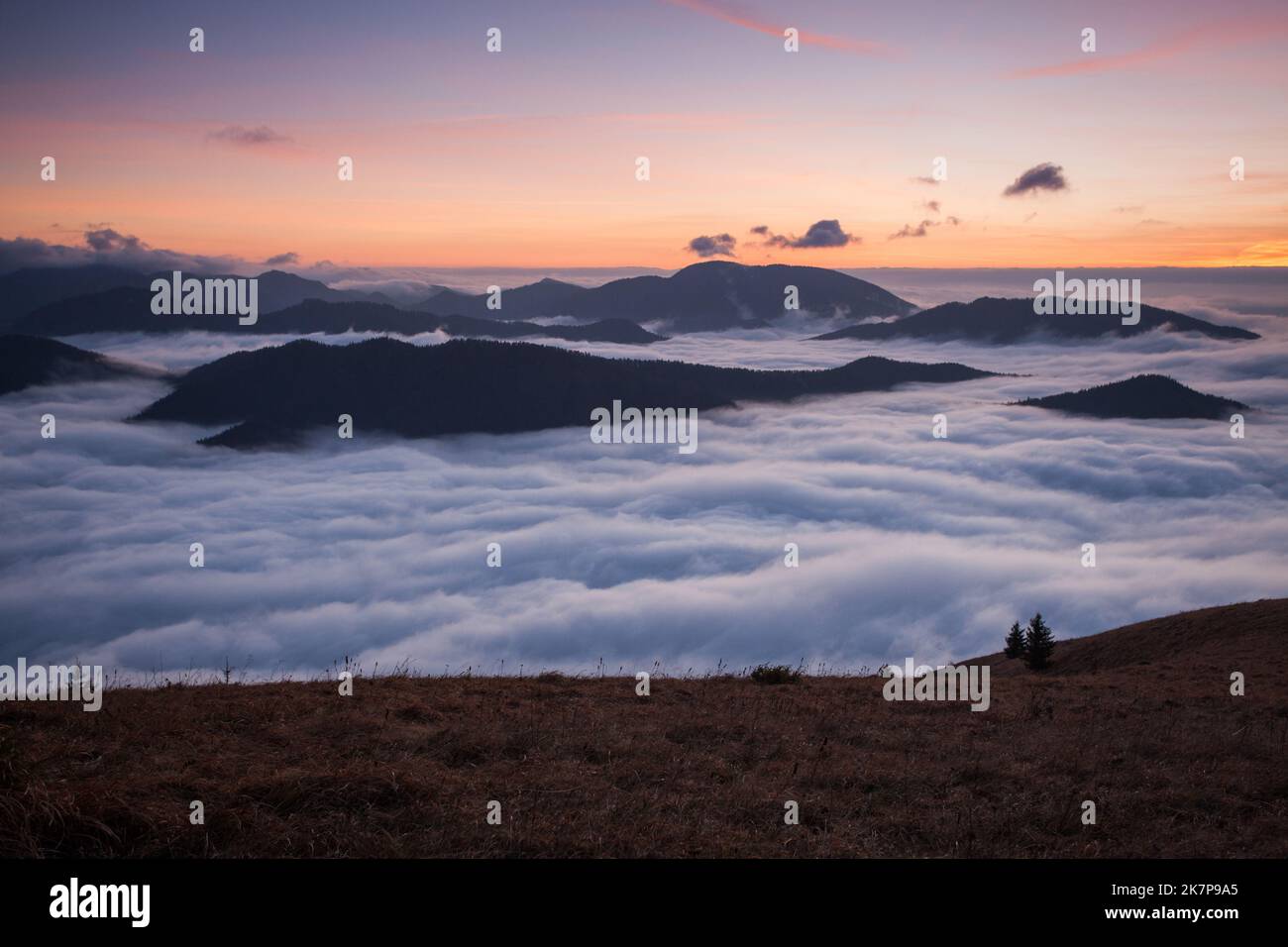 Sunset hidden behind clouds and fog over hills, bright yellow sun on colorful cloudscape, blue violet orange sky. Stock Photo