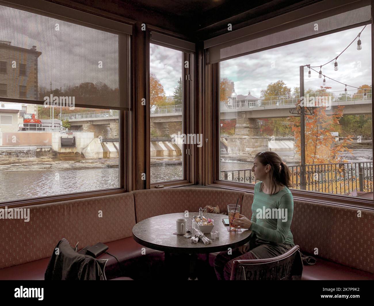 A girl enjoys a drink in front of a full corner fall view; retro, vintage image of dining out. Stock Photo