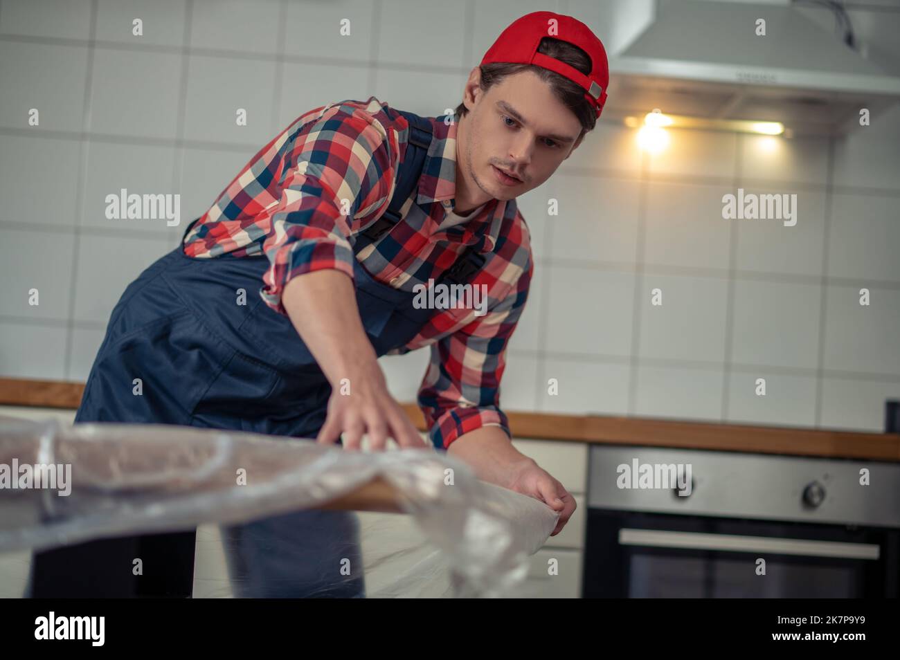 Concentrated young serviceman wrapping the wooden tabletop Stock Photo