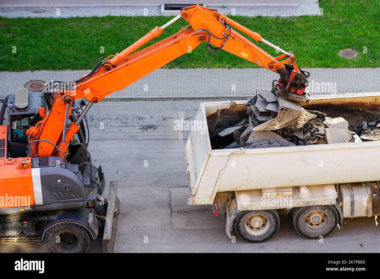 an-orange-excavator-with-a-bucket-loads-the-old-pieces-of-asphalt-into