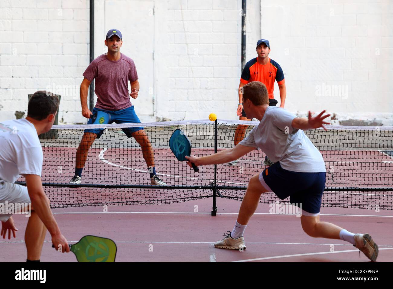 A group of white male millenials play pickleball on a basketball court with dual pickleball and basketball court striping in Manhattan, New York City Stock Photo