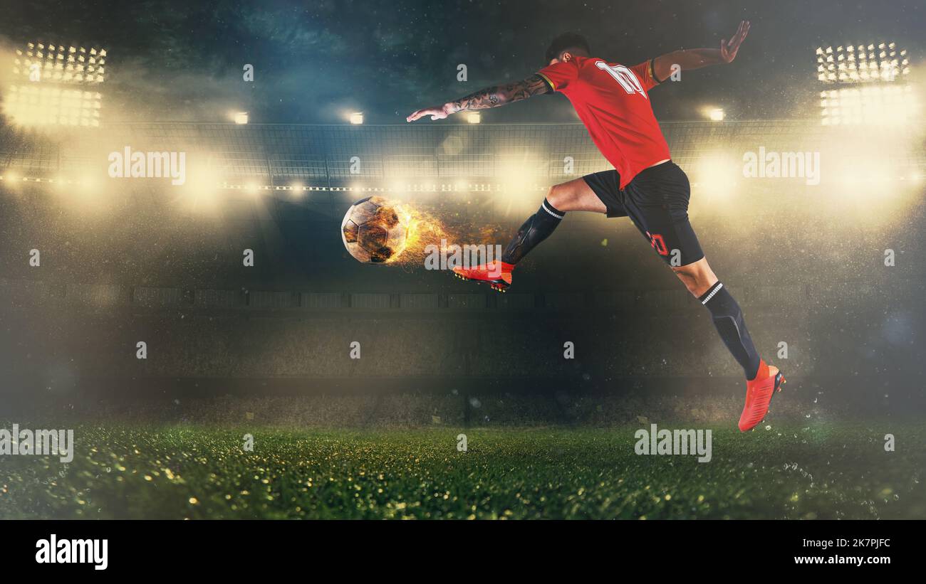 Soccer scene at night match with player in a red uniform kicking a fiery ball with power Stock Photo