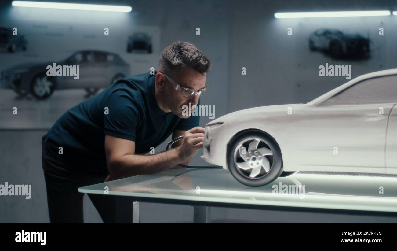 Senior automotive design engineer uses a rotary tool for perfecting the rake sculpture of a car model in a high tech company. Engineer wearing safety goggles works in an automotive company. Stock Photo