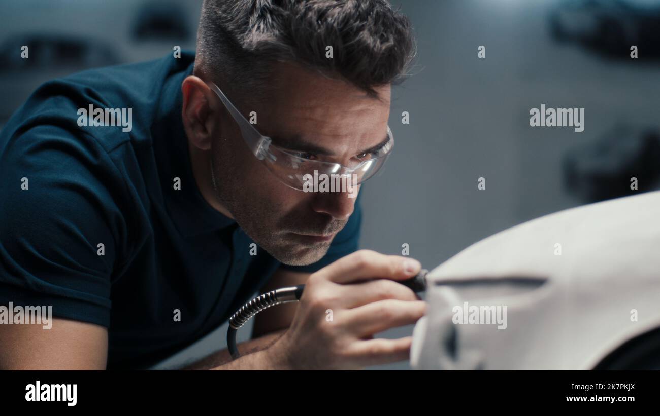 Senior automotive design engineer uses a rotary tool for perfecting the rake sculpture of a car model in a high tech company. Engineer wearing safety goggles works in an automotive company. Stock Photo