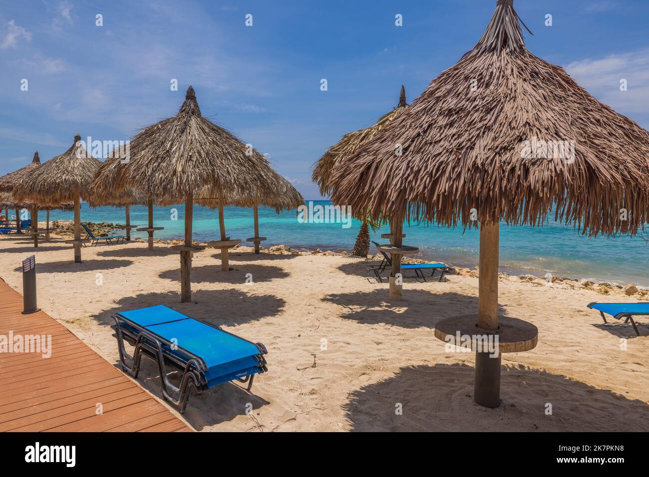 Beautiful view of sun beds and umbrellas on sandy beach on turquoise water surface and blue sky background. Aruba. Stock Photo