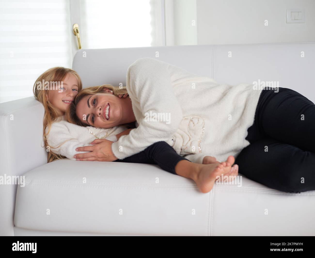 young mother and daughter lying on white sofa Stock Photo