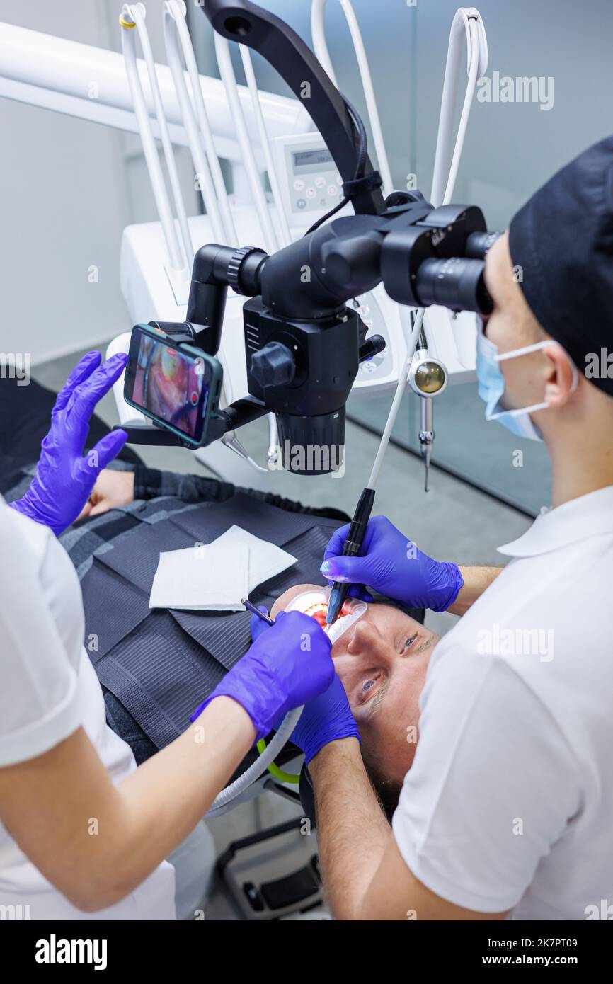 A young dentist looks at the patient's teeth with a dental microscope ...