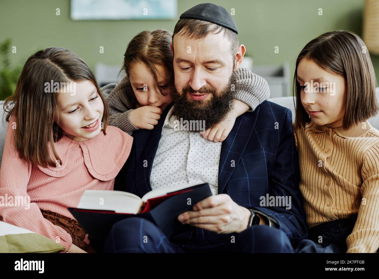 Portrait of orthodox Jewish man wearing kippah while reading book to three children Stock Photo