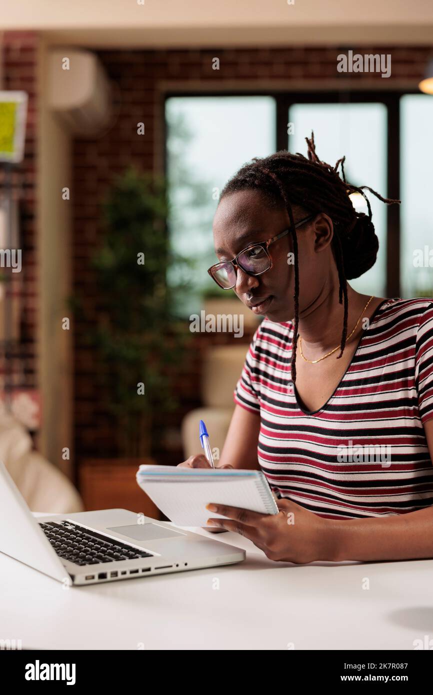 Serious student watching webinar, reading educational materials on laptop, taking notes. Online