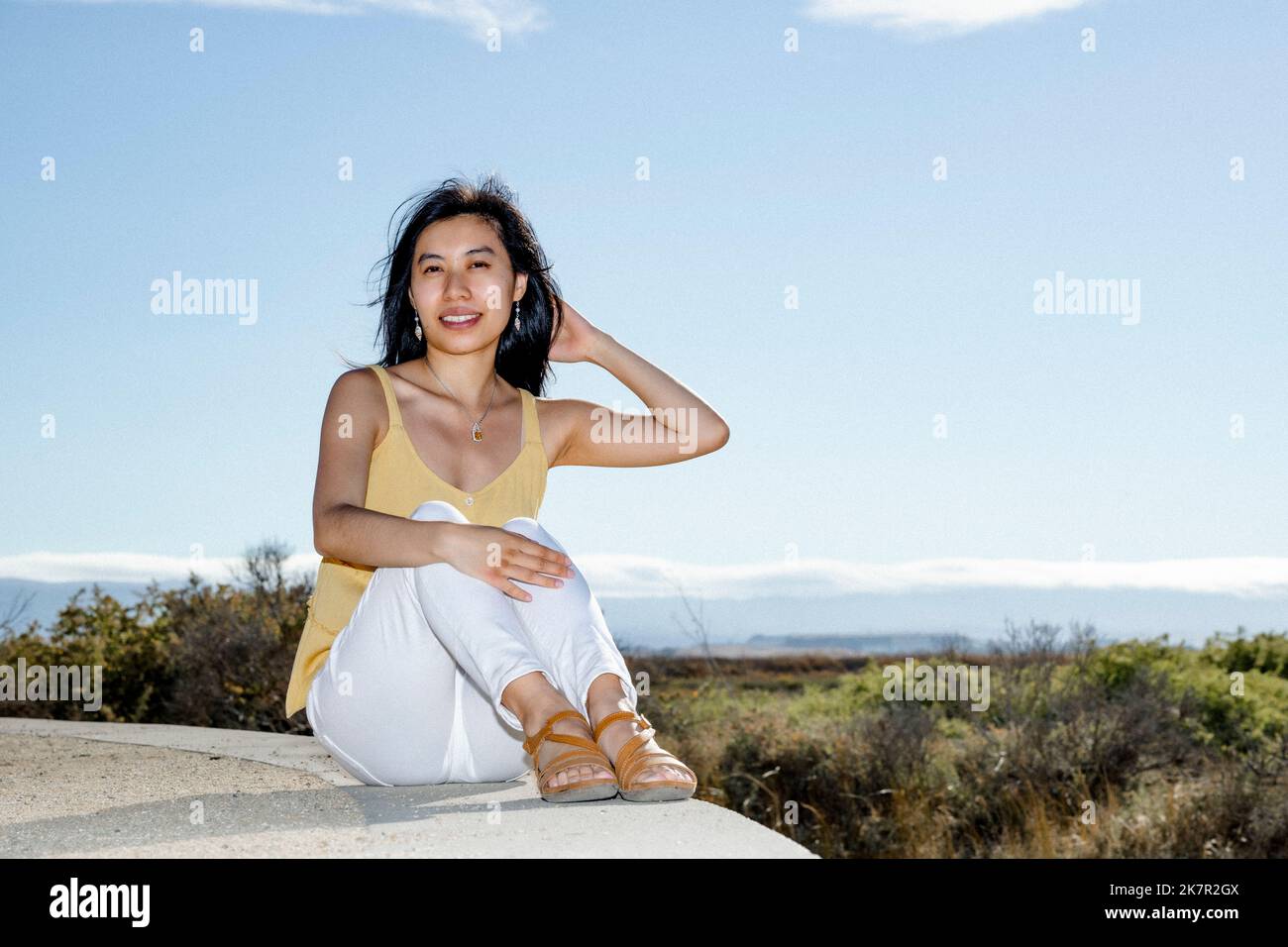 Young Woman Sitting on a Wall Overlooking a Marshland Stock Photo
