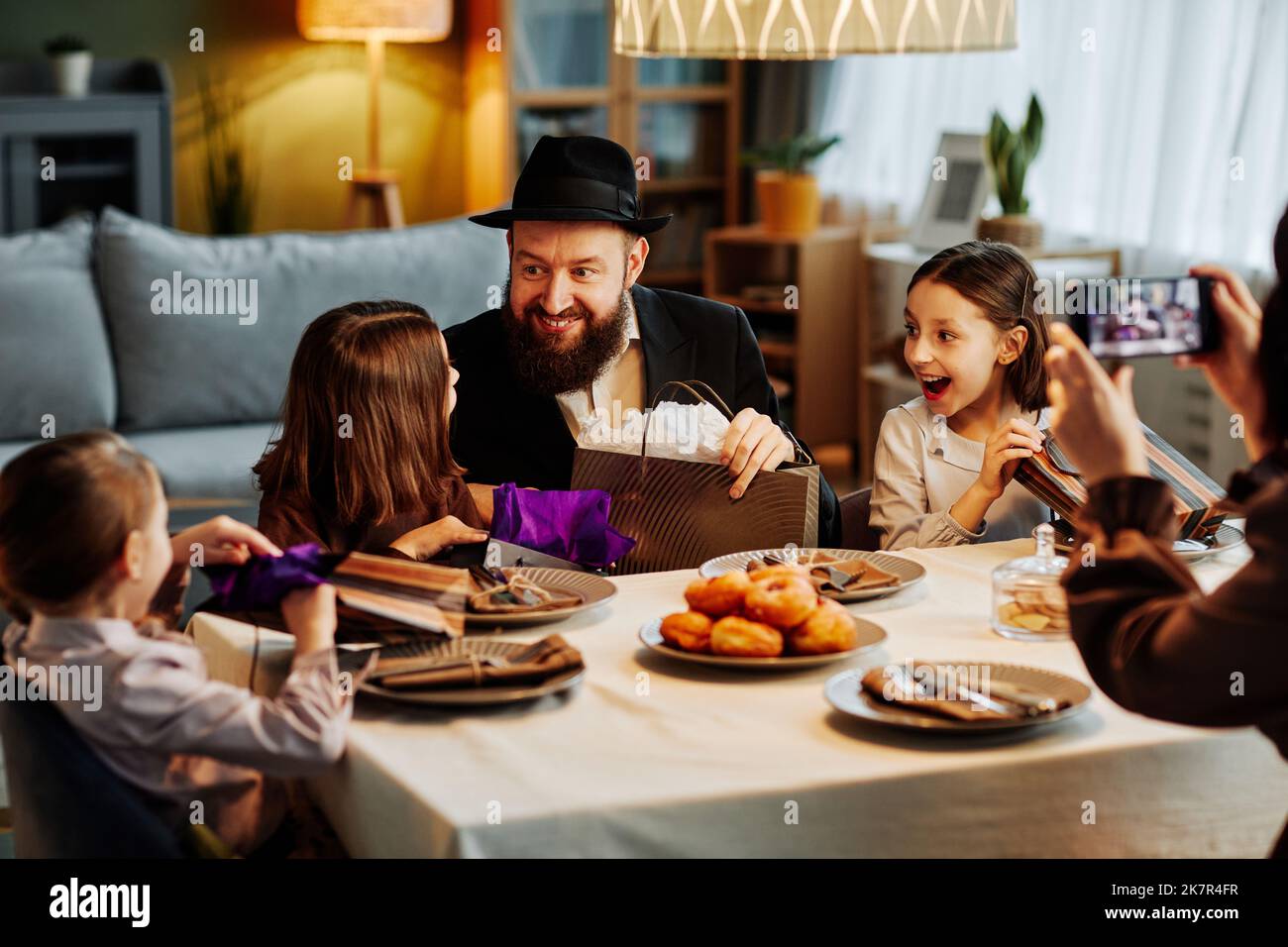 Portrait of modern jewish family sharing gifts at dinner table in cozy
