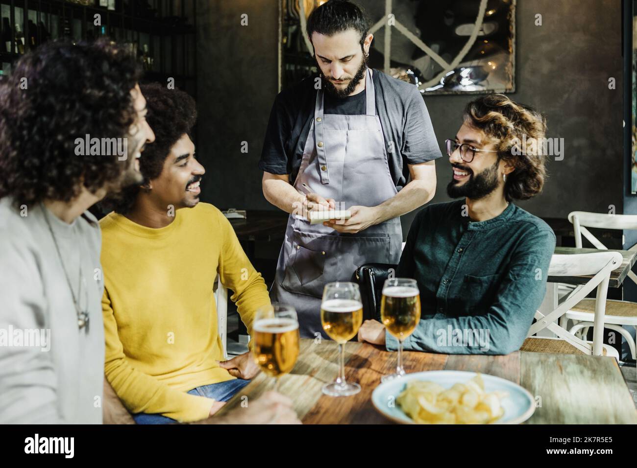 Young waitress taking order from multiracial male friends at restaurant Stock Photo
