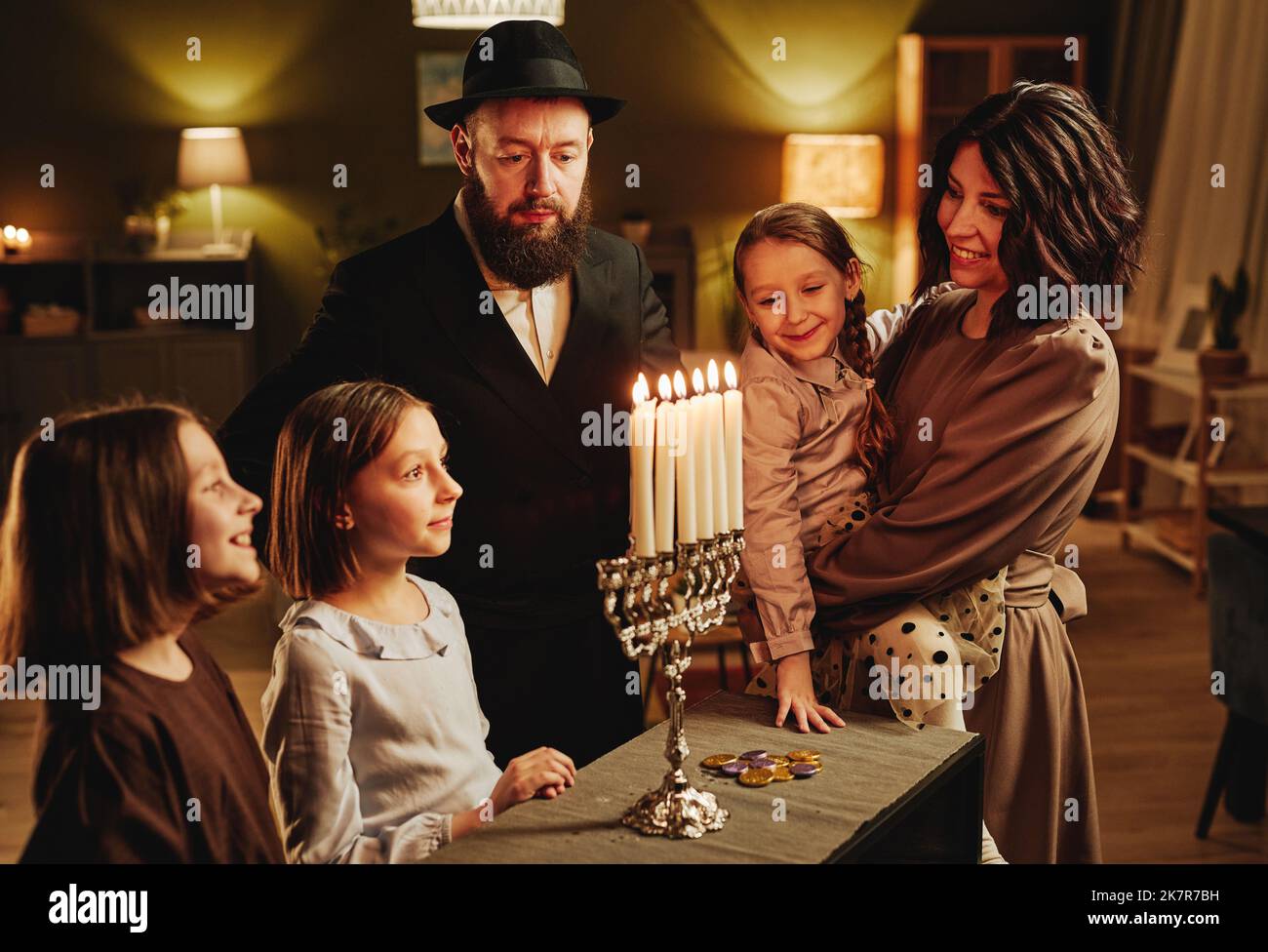 Portrait of modern jewish family looking at silver menorah candle during Hanukkah celebration in