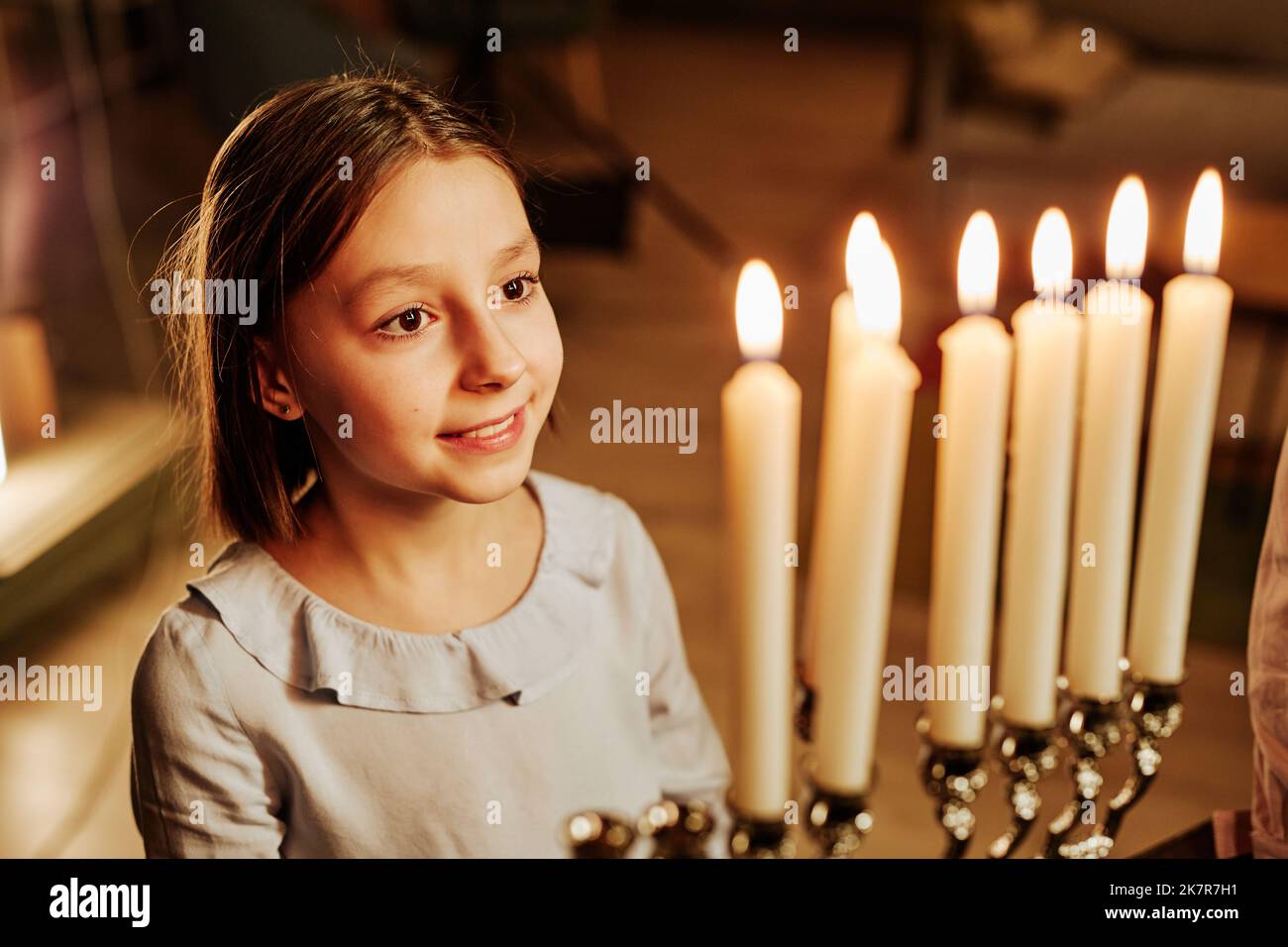 High angle portrait of smiling jewish girl looking at Menorah candle during Hanukkah celebration Stock Photo