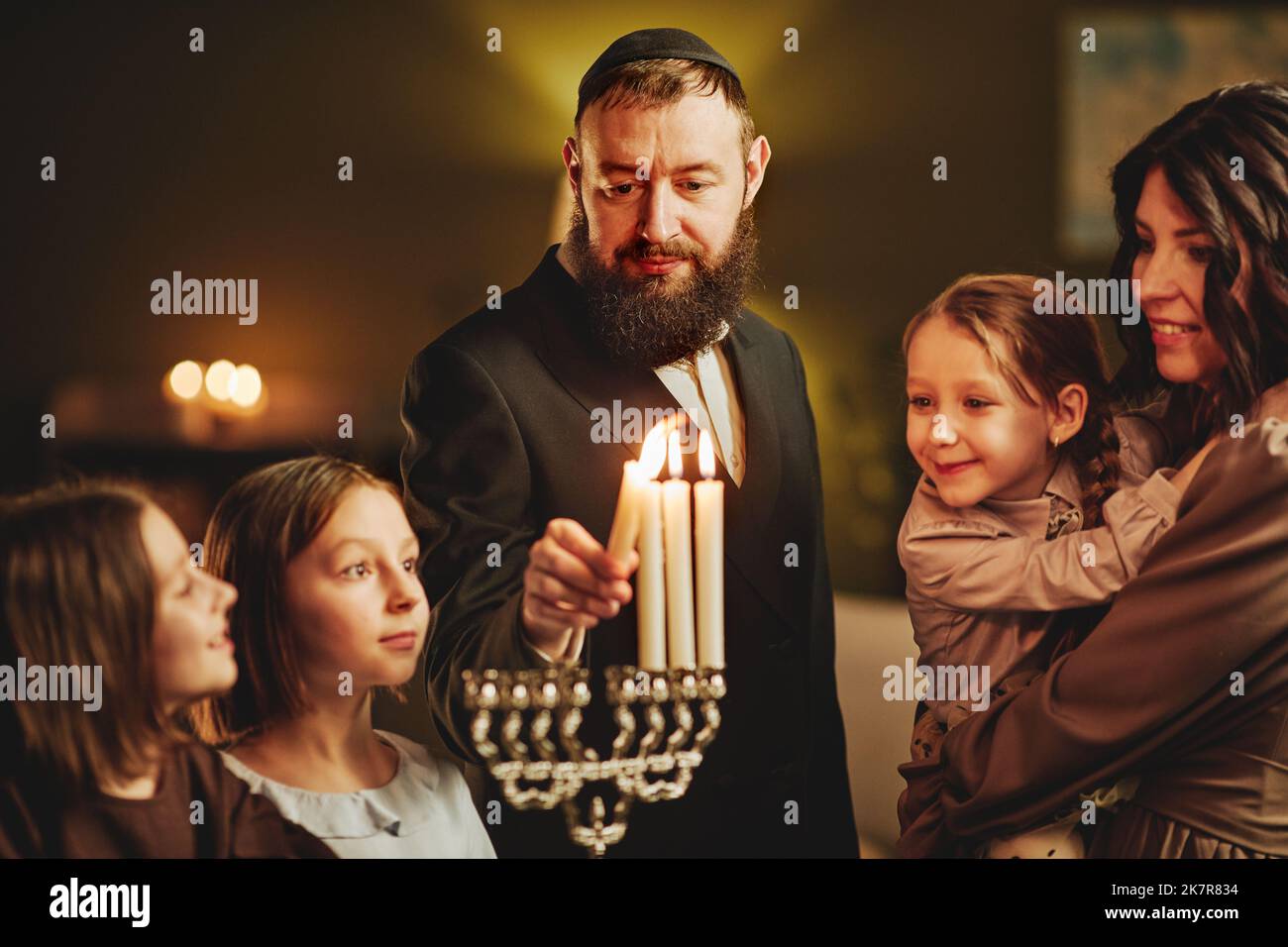 Portrait of orthodox jewish man lighting menorah candle with family during Hanukkah celebration Stock Photo