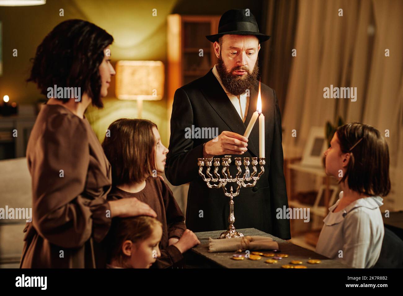 Portrait of orthodox jewish man with family lighting menorah candle during Hanukkah celebration Stock Photo