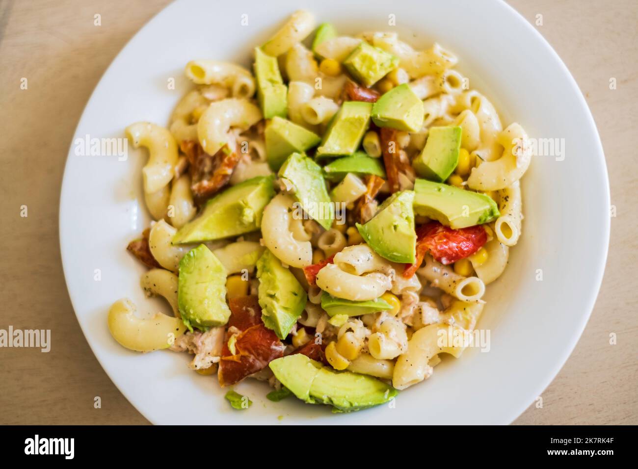 A cold pasta salad of large elbow macaroni, sliced avocados, red bell peppers and yellow corn with a light mayonaise dressing in a white dish. USA Stock Photo