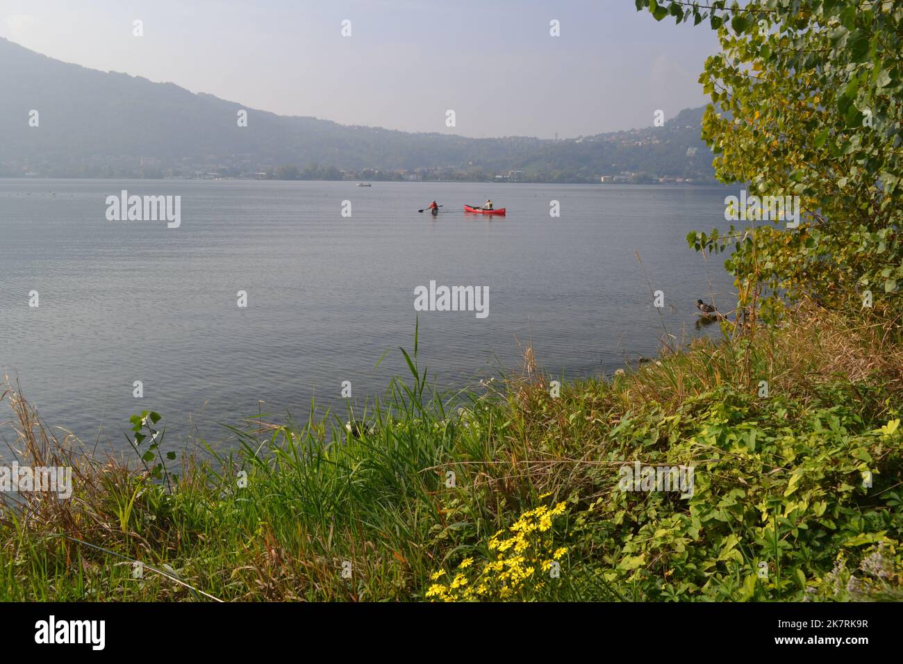 Lecco, Italy - October 17, 2022: Beautiful autumn view on Lake Garlate. Rowers in canoes paddle in the distance. Stock Photo