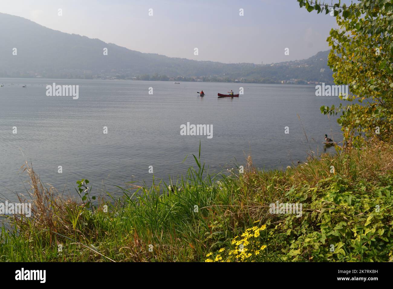 Lecco, Italy - October 17, 2022: Beautiful autumn view on Lake Garlate. Rowers in canoes paddle in the distance. Stock Photo