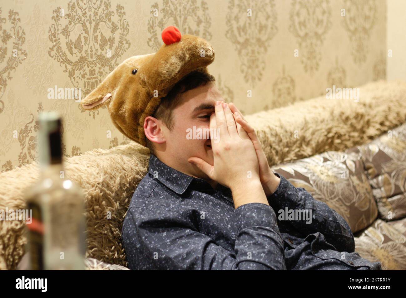 Defocus happy sleeping alcoholic. Drunk man with empty wine bottle, sleeping smiling and hiding face. Man in bear mask. Alcoholism. Funny holiday. Out Stock Photo