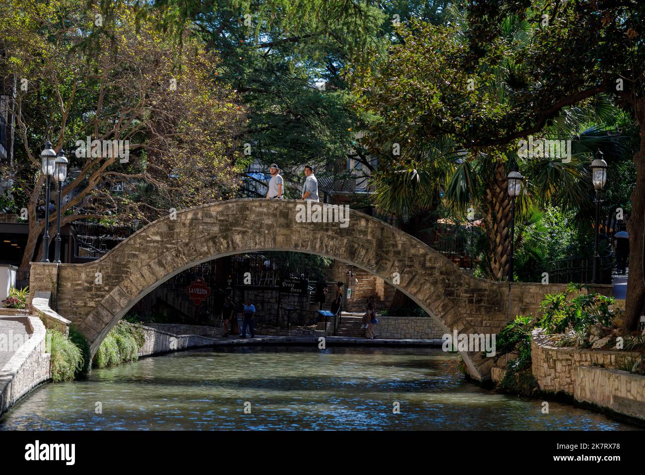People walk across a metal bridge over the San Antonio