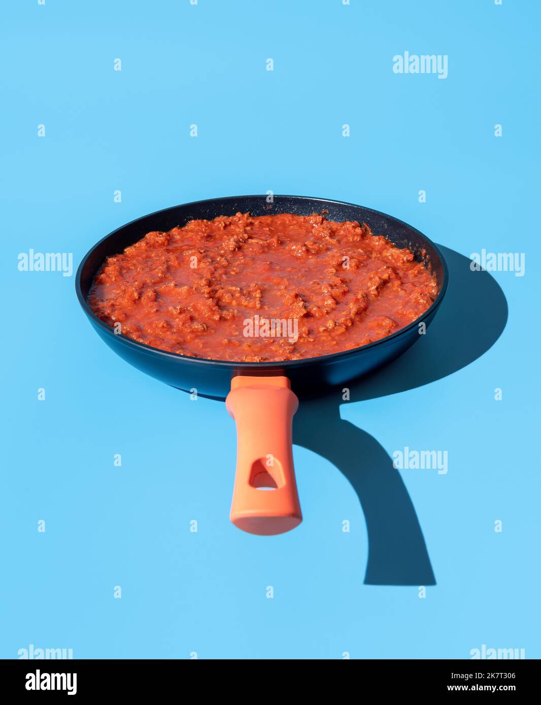 Pan with classic italian bolognese sauce minimalist on a blue table. Delicious ragu sauce pot in bright light on a vibrant-colored background. Stock Photo