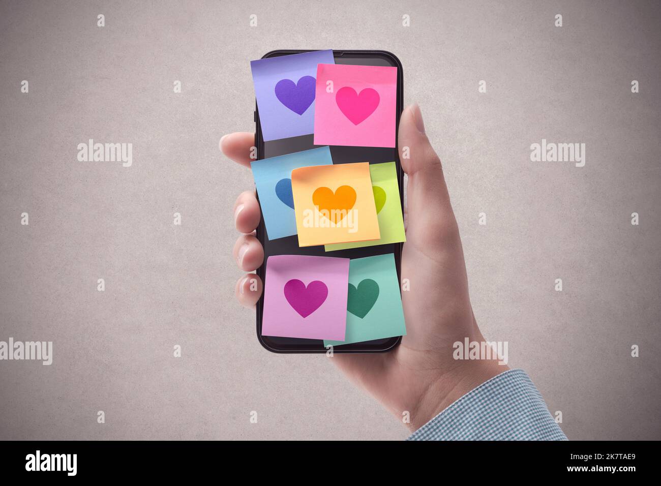 Woman holding a smartphone and lots of sticky notes with hearts on the display, relationships and communication concept, POV shot Stock Photo