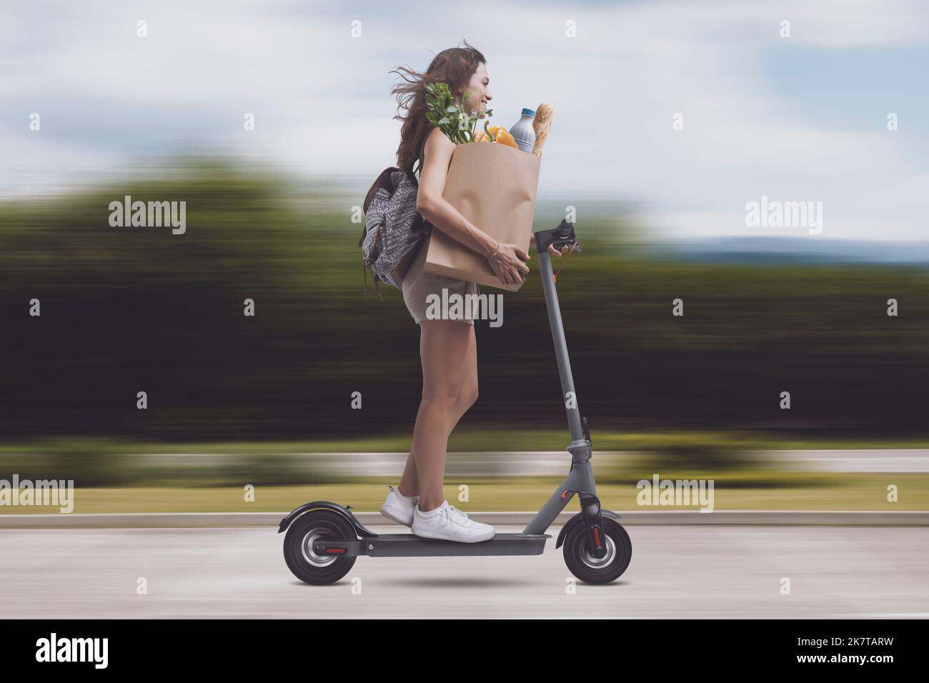 Young woman carrying a paper bag with groceries and riding a fast electric scooter, grocery shopping concept Stock Photo
