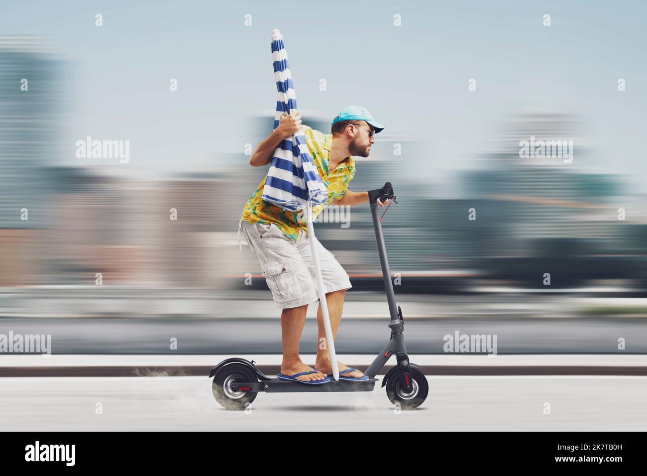 Man riding an electric scooter and holding a beach umbrella, he is going to the beach Stock Photo