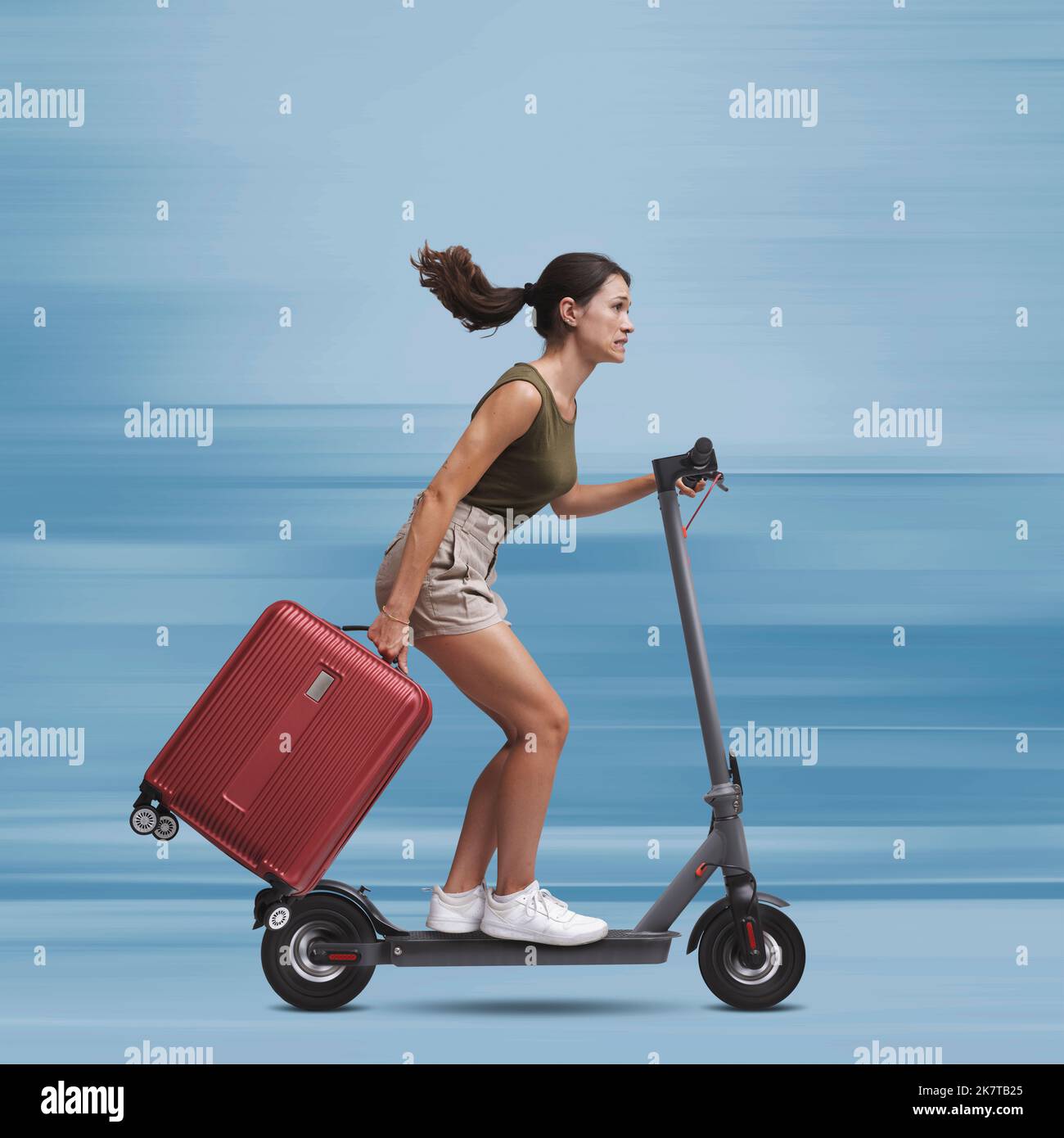 Tourist woman riding a fast electric scooter and carrying a trolley bag, she is late, sustainable mobility concept Stock Photo