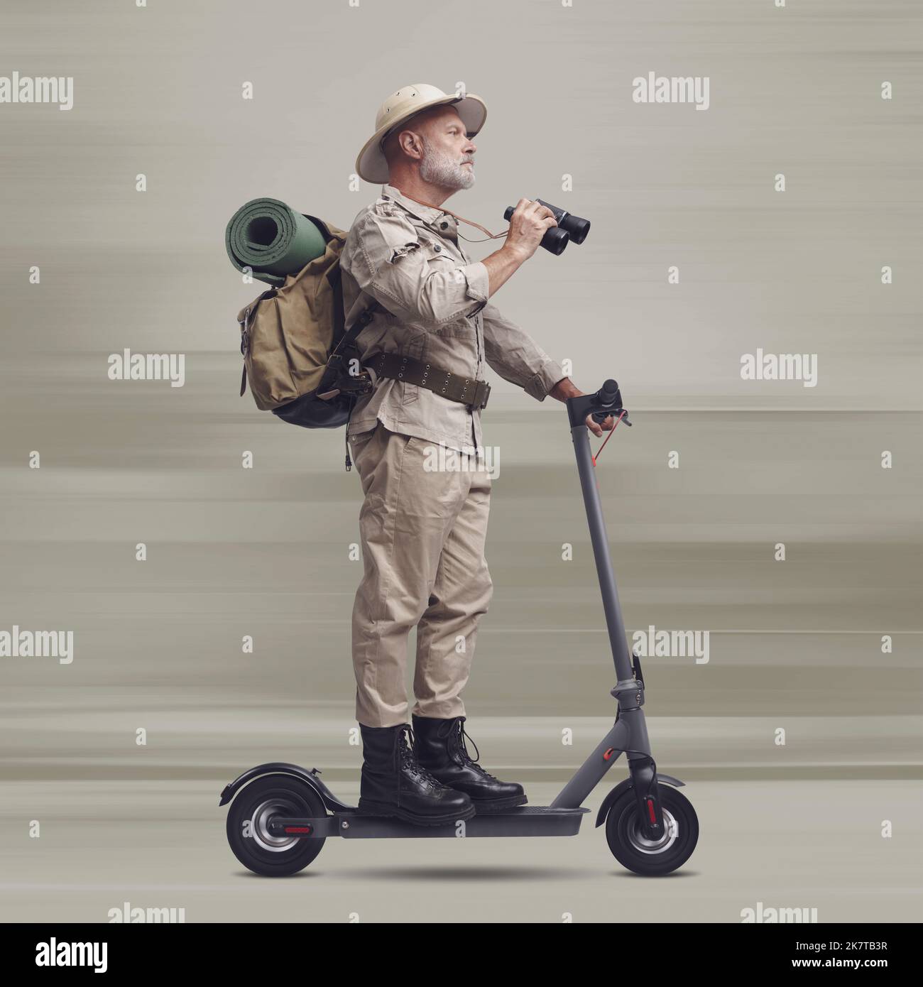 Funny explorer riding a fast electric scooter and holding binoculars Stock Photo
