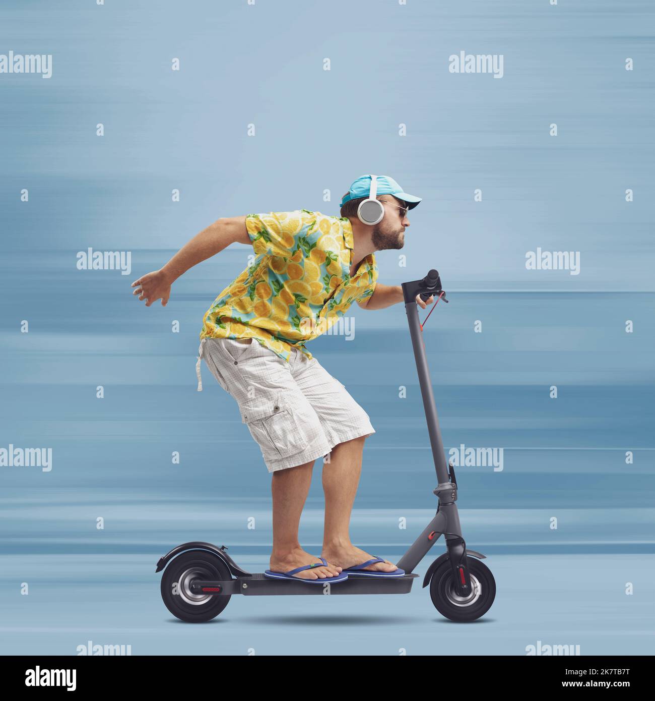 Cool stylish man wearing a colorful beach shirt and riding a fast eco-friendly electric scooter, smart mobility concept Stock Photo