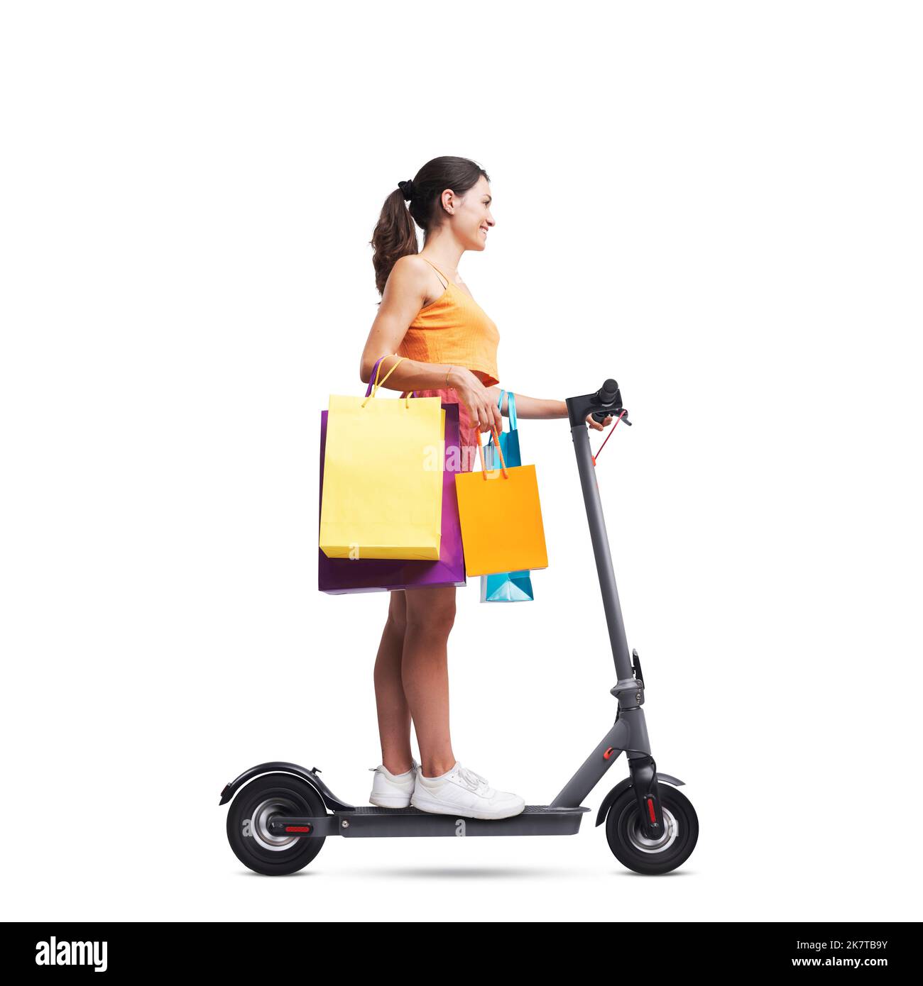 Fashionable woman holding shopping bags and riding an electric scooter, isolated on white background Stock Photo