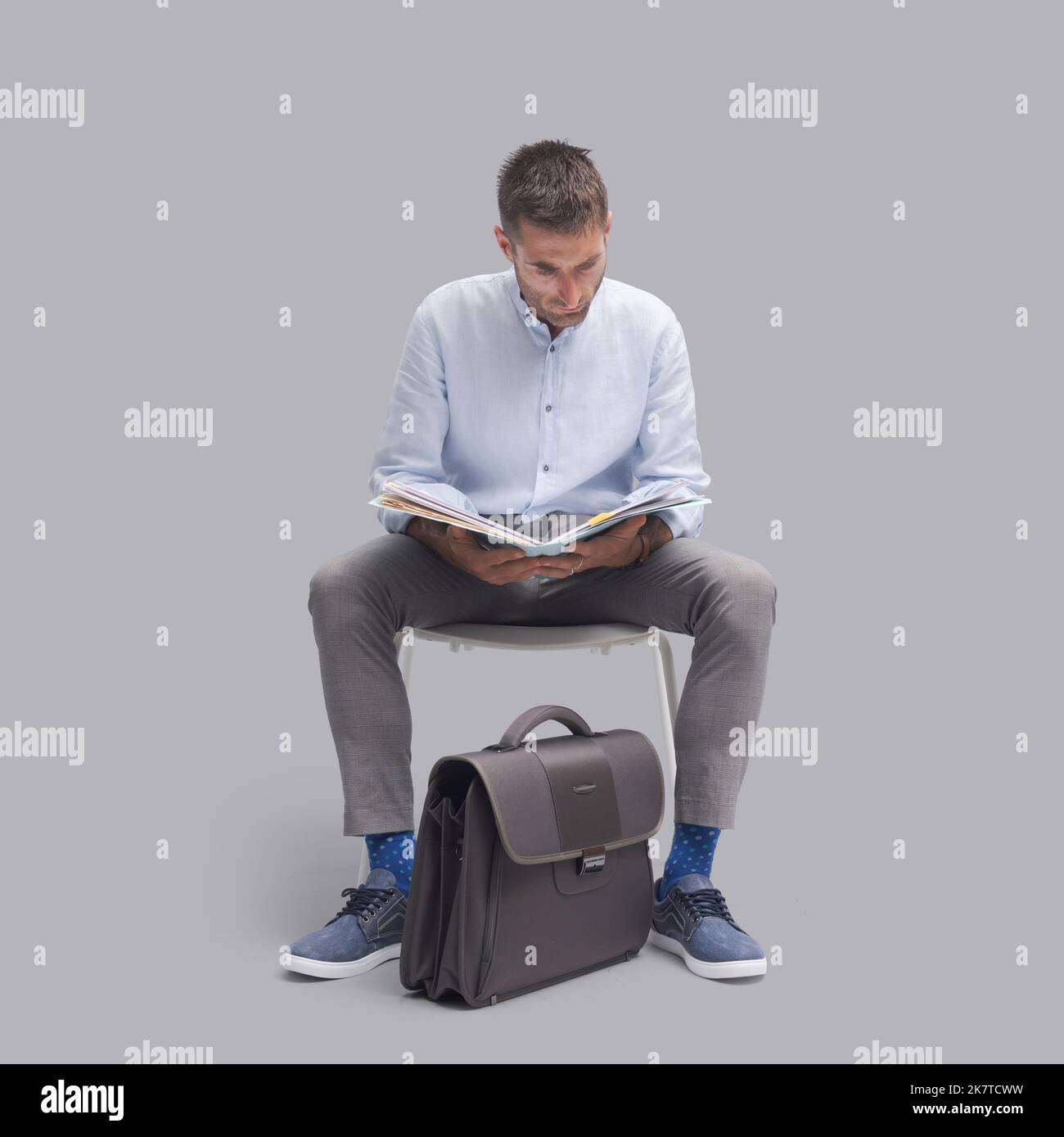 Man sitting on a chair and checking paperwork, he is waiting for a meeting Stock Photo