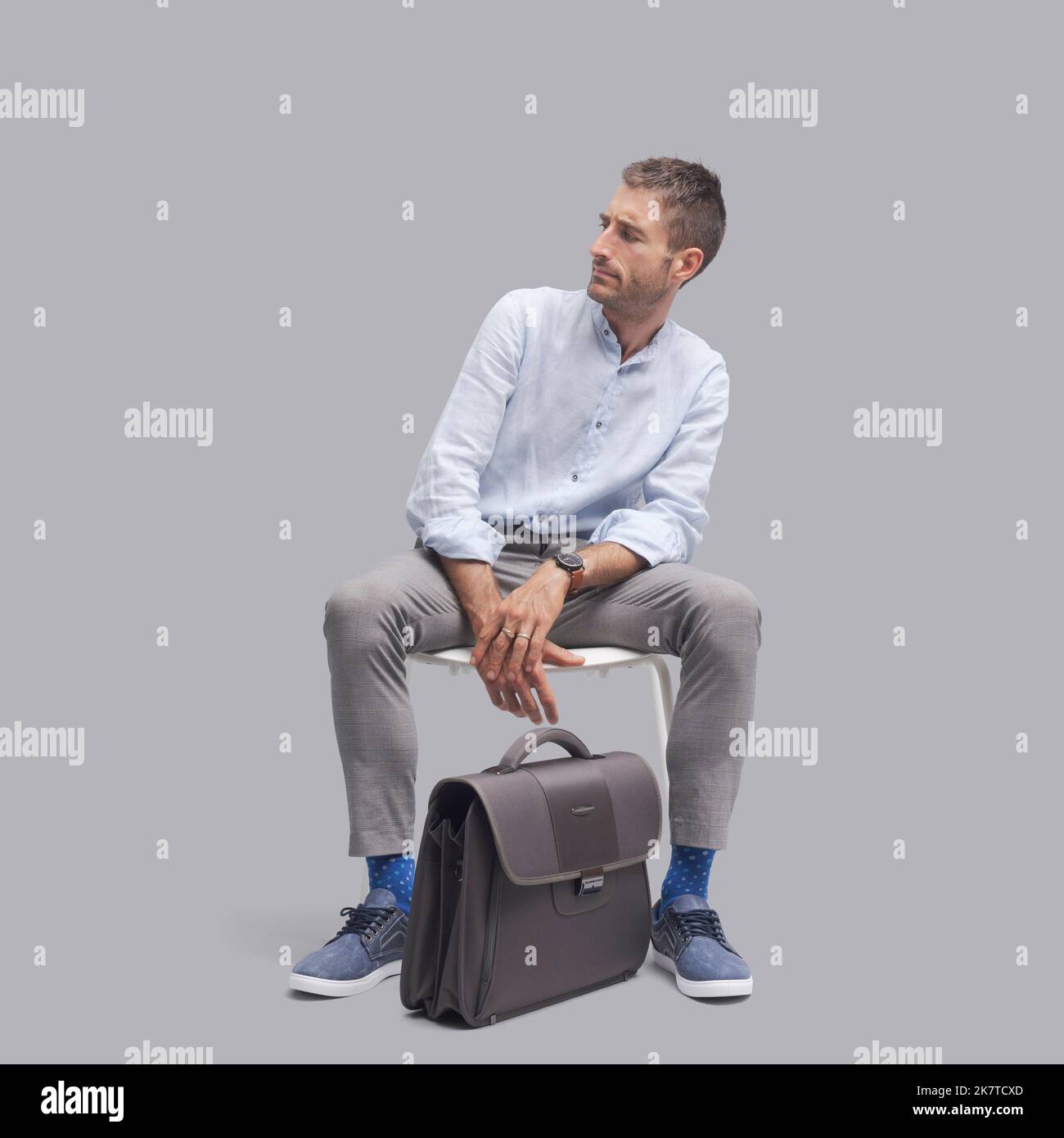 Disappointed man sitting on a chair and looking at his side, he is waiting for a job interview Stock Photo