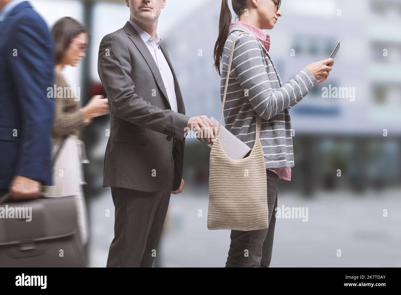 Robber stealing a wallet in the city street, the victim is distracted and using her smartphone Stock Photo