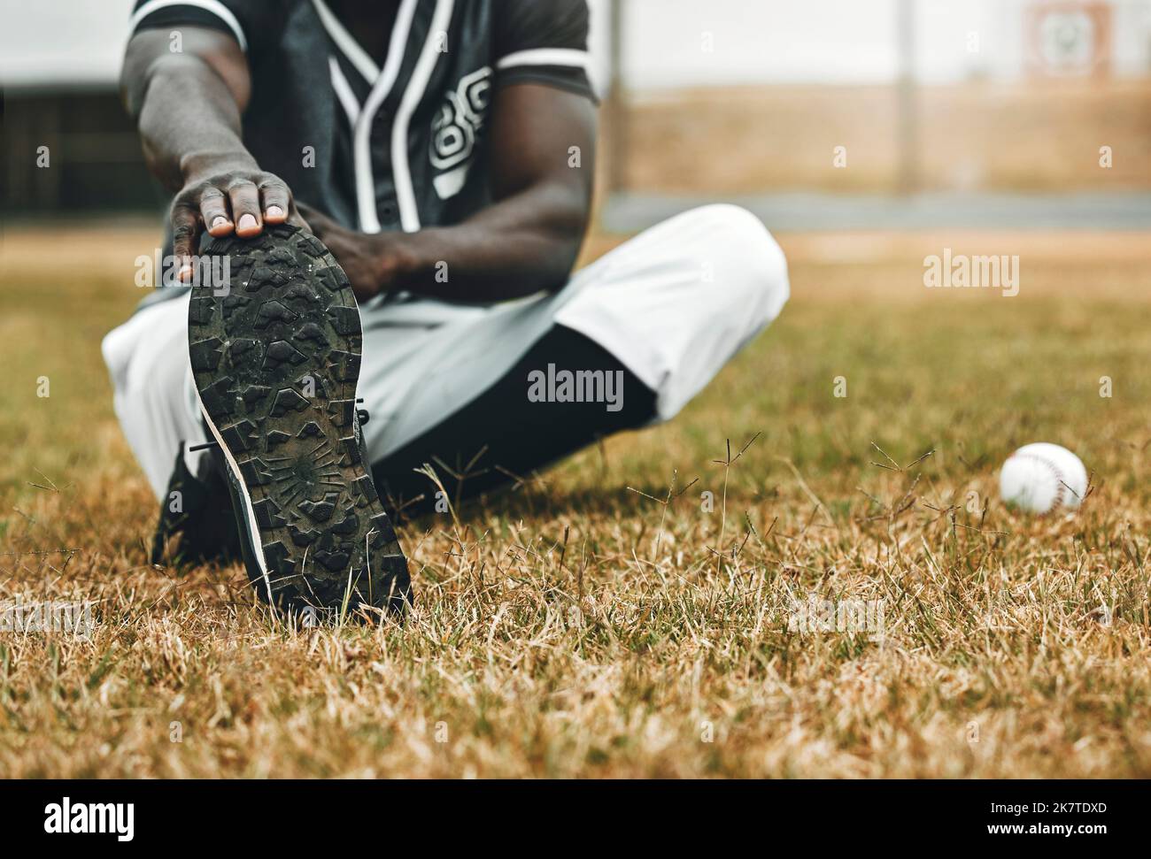 Baseball player, stretching legs and athlete black man on sports field doing warm up exercise, workout and practice for match. Fitness male touch feet Stock Photo