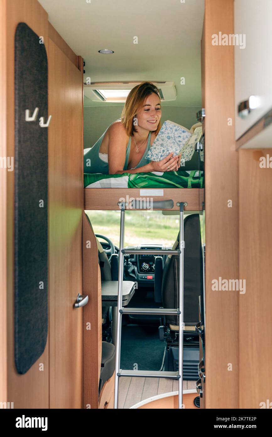 Woman lying on camper van bunk bed reading book Stock Photo