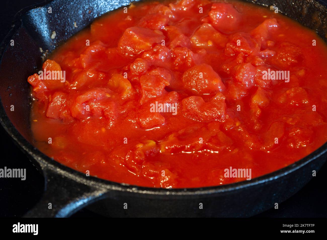 Cooking chopped tomatoes in a cast iron frying pan, on an electric hob stove Stock Photo