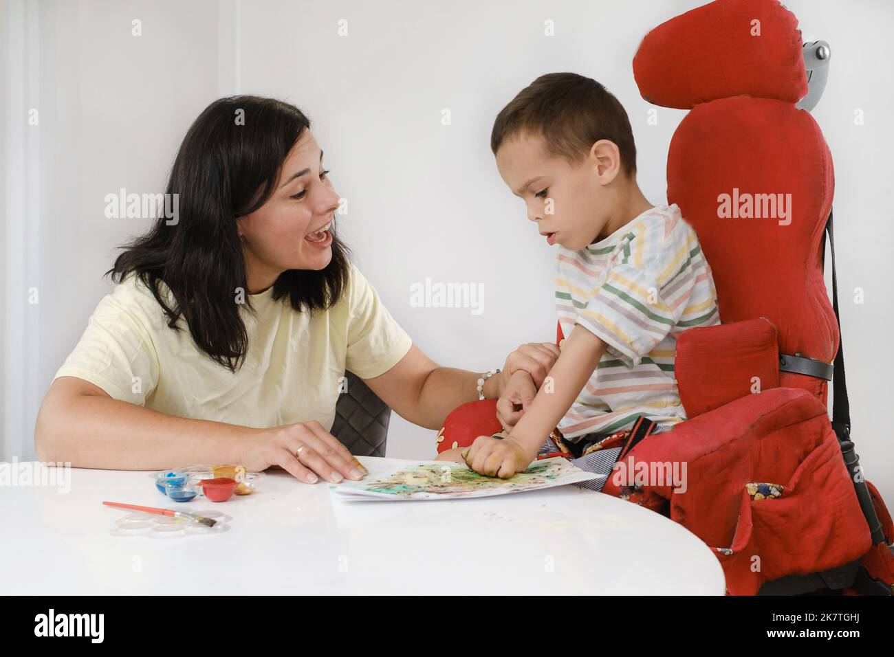 Child with cerebral palsy painting with fingers and hands boy that has health problems developing fine motor skills Education for children with mental Stock Photo