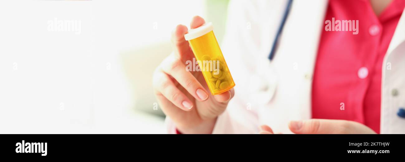 Doctor hold plastic container filled with tiny white pills, female intern advertises medication Stock Photo