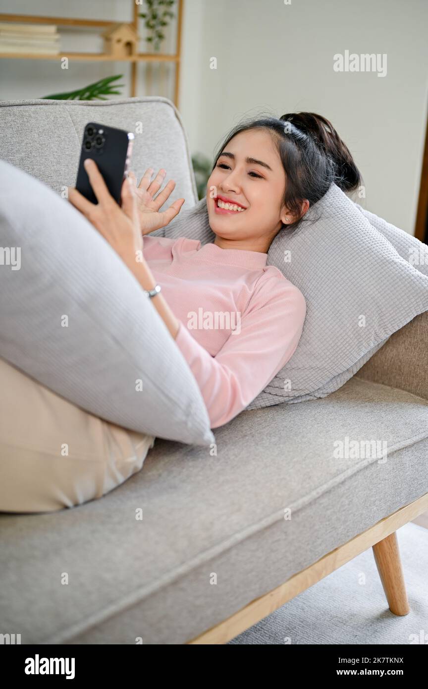 Portrait, Charming and pretty young Asian female in casual clothes spending her free time on video call, talking with her friends on the phone while r Stock Photo