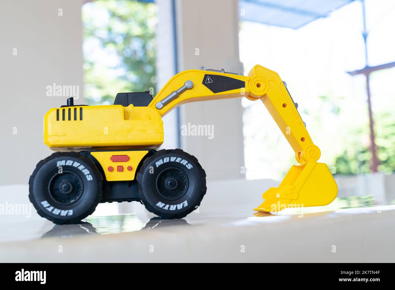 Backhoe loader, yellow construction toy vehicle with articulated parts built with sturdy plastic is placed on a table. Stock Photo