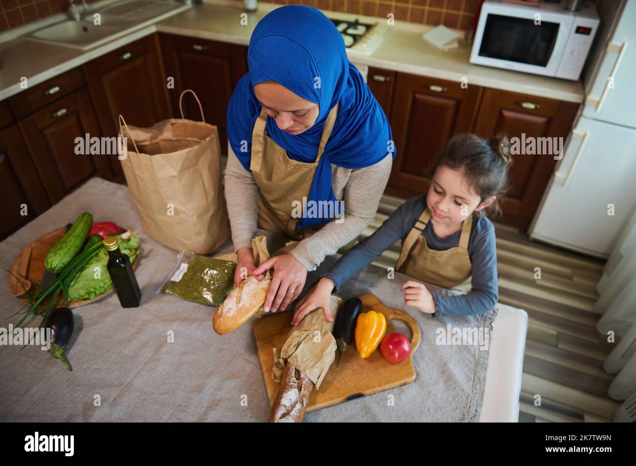 Top view. Muslim woman, loving mom with little daughter unpacking food from supermarket bag together for preparing meal Stock Photo